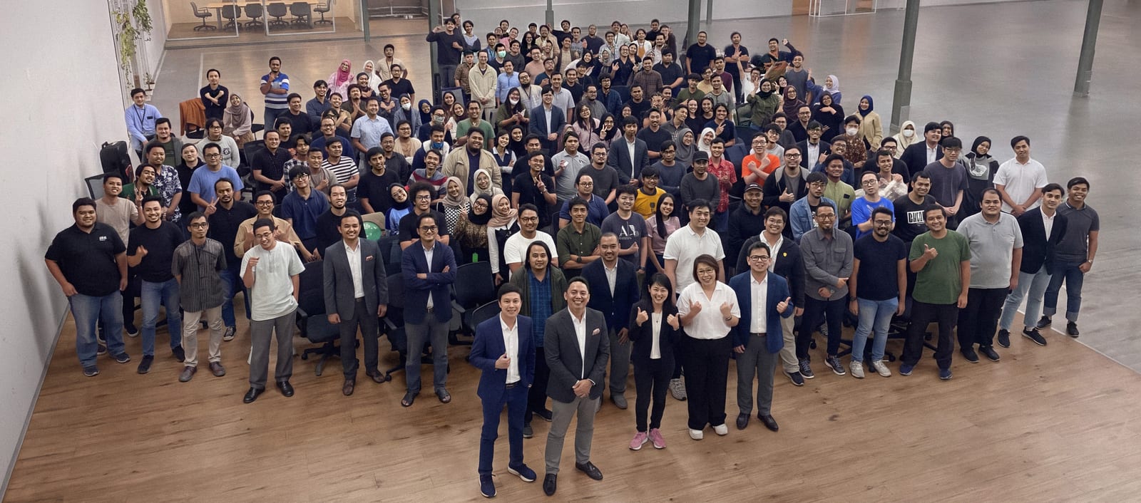 Around 200 members of the Xtremax team gathered together in an open office hall, smiling up at the camera, with leadership in the front row